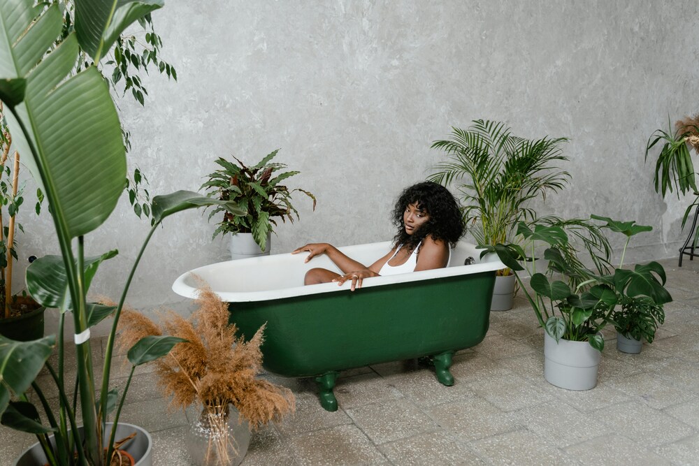 Woman relaxing in a vintage bathtub surrounded by tropical indoor plants like Monstera, Palm, and Calathea